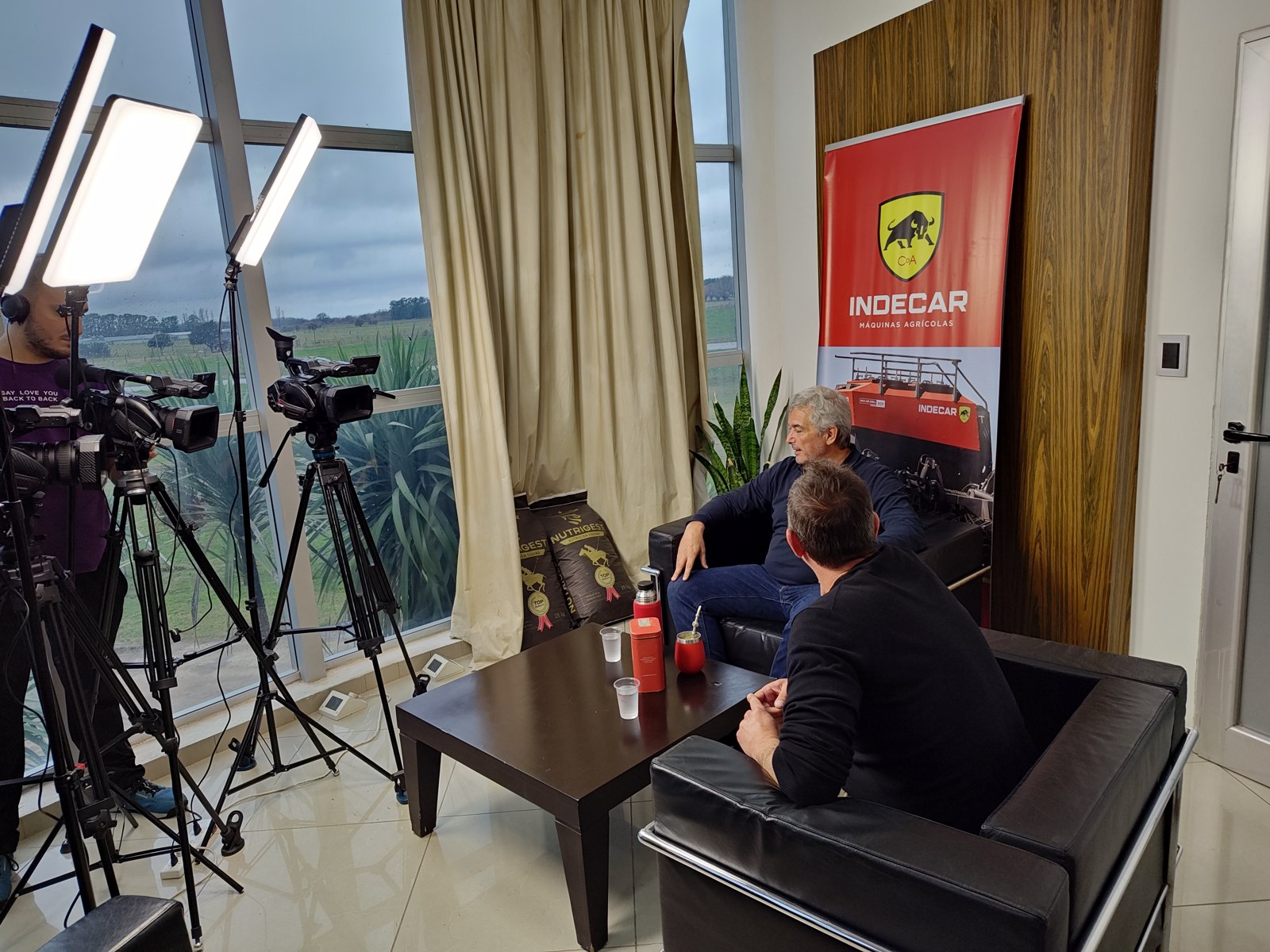 Entrevista en la fábrica de Indecar, con cámaras, iluminación y una bandera de la marca.
